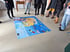 Personen stehen um eine große, bunte Bodenkarte mit blauen Meeren und gelben Landmassen.