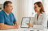 Eine Ärztin zeigt einem sitzenden Mann auf einem Tablet mit der Aufschrift "Health Plan" ein Bild von Lungen.