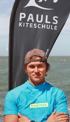 Kitelehrer Steffen mit Cap vor dem Meer und der Flagge von Pauls Kiteschule in Brouwersdam