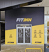 Eingang zum Fitnessstudio FitINN mit schwarzen und gelben Wänden, verglaster Tür und der Aufschrift "FITINN".