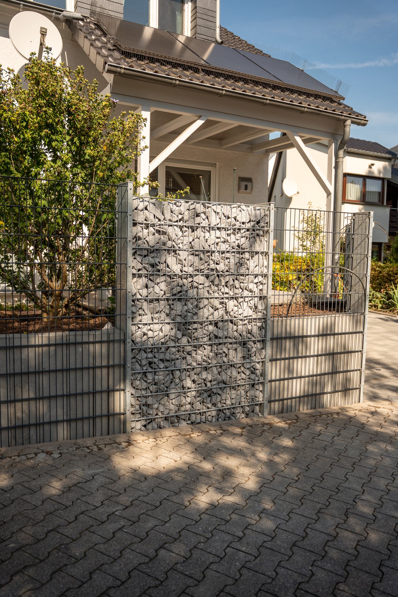 Von Calis Gartenbau gebauter Sichtschutz aus Gabionen und grauen Doppelstabmatten vor einem Wohnhaus mit Solaranlage