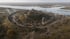 A fortified hilltop settlement with wooden buildings surrounded by a circular palisade near a river.