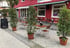 Ein Bürgersteig-Café mit roter Fassade, leeren Tischen, Stühlen und grünen Topfpflanzen im Außenbereich.