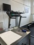 Ein Laufband mit Monitor, ein Labortisch mit Geräten und einem Formular in einem Fitnessraum.