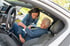 Eine jüngere Frau hilft einer Seniorin beim Einsteigen auf den Beifahrersitz eines Autos.