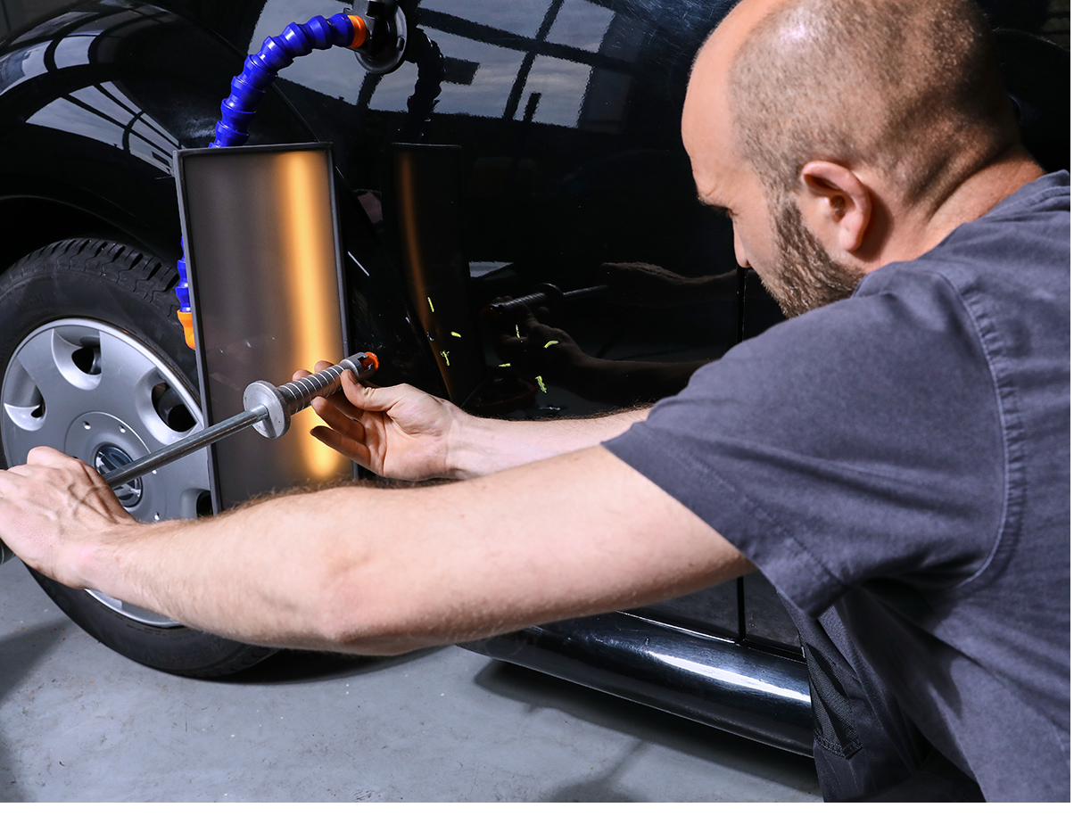 Techniker drückt eine Delle am Fahrzeug heraus