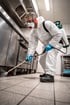 Schädlingsbekämpfer in Schutzkleidung sprüht Insektizid in einer gewerblichen Küche auf den Boden.