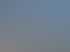 Ein Kran hebt ein langes, dunkles Brückensegment mit roten Hebegurten unter blauem Himmel mit Wolken an.