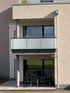 Modernes Apartmentgebäude mit Balkon im Obergeschoss und Terrasse mit Möbeln im Erdgeschoss.