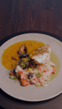 Eine Portion Fisch mit Muscheln in gelber Sauce, serviert mit Reis und Gemüse, auf einem hellen Teller.