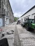 Pflasterarbeiten in einem Hinterhof mit einem grünen Radlader, Baumaschinen und frisch verlegten Verbundsteinen.