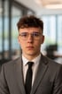 Christoffer Zinke mit lockigen Haaren, Brille, grauem Anzug, weißem Hemd und schwarzer Krawatte.