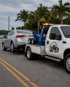 Towing Port Charlotte wheel lift tow truck towing a sedan on a palm-lined road for roadside assistance.