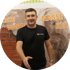 Mann in schwarzem T-Shirt mit Logo bietet Händedruck an vor Wand mit Text "FEUCHTE WÄNDE" und "NASSE KELLER".