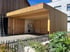 Neues Holzcarport mit Flachdach, links eine offene Holztür, rechts ein Zaun und Pflanzen.