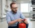Mann mit Brille prüft einen roten Feuerlöscher in einem Industrieraum.