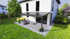 Moderne Terrassenüberdachung mit Glasdach und schwarzem Rahmen an einem weißen Haus mit Garten.