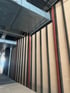 Rohbau einer Wand mit vertikalen schwarzen Metallprofilen, roten Stützen und einem Lüftungskanal aus Zinkblech an der Decke.