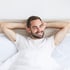 Smiling man in a white t-shirt relaxing in bed, representing Erectile Dysfunction relief.