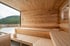 Moderne Holzsauna mit Panoramafenster, Holzbänken und Blick auf bewaldete Berge.