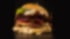 Ein unscharfer Burger mit Salat, Käse und Fleisch auf einem dunklen Hintergrund.