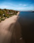 Luftaufnahme vom Elbstrand in Hamburg mit bewaldetem Hang, Wohnhäusern und den Krananlagen des Hafens im Hintergrund.