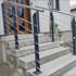 Betontreppe mit Edelstahlgeländer und dunkelblauen Pfosten vor einer Haustür.