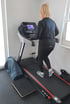 Blonde Person auf einem Laufband mit der Anzeige 4.6, ein Handtuch auf einem Hocker daneben.
