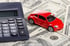 Ein rotes Spielzeugauto steht neben einem Taschenrechner auf mehreren 100-US-Dollar-Geldscheinen.