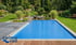 Blauer, rechteckiger Pool mit Abdeckung in einem Garten mit Teich und Rasen.