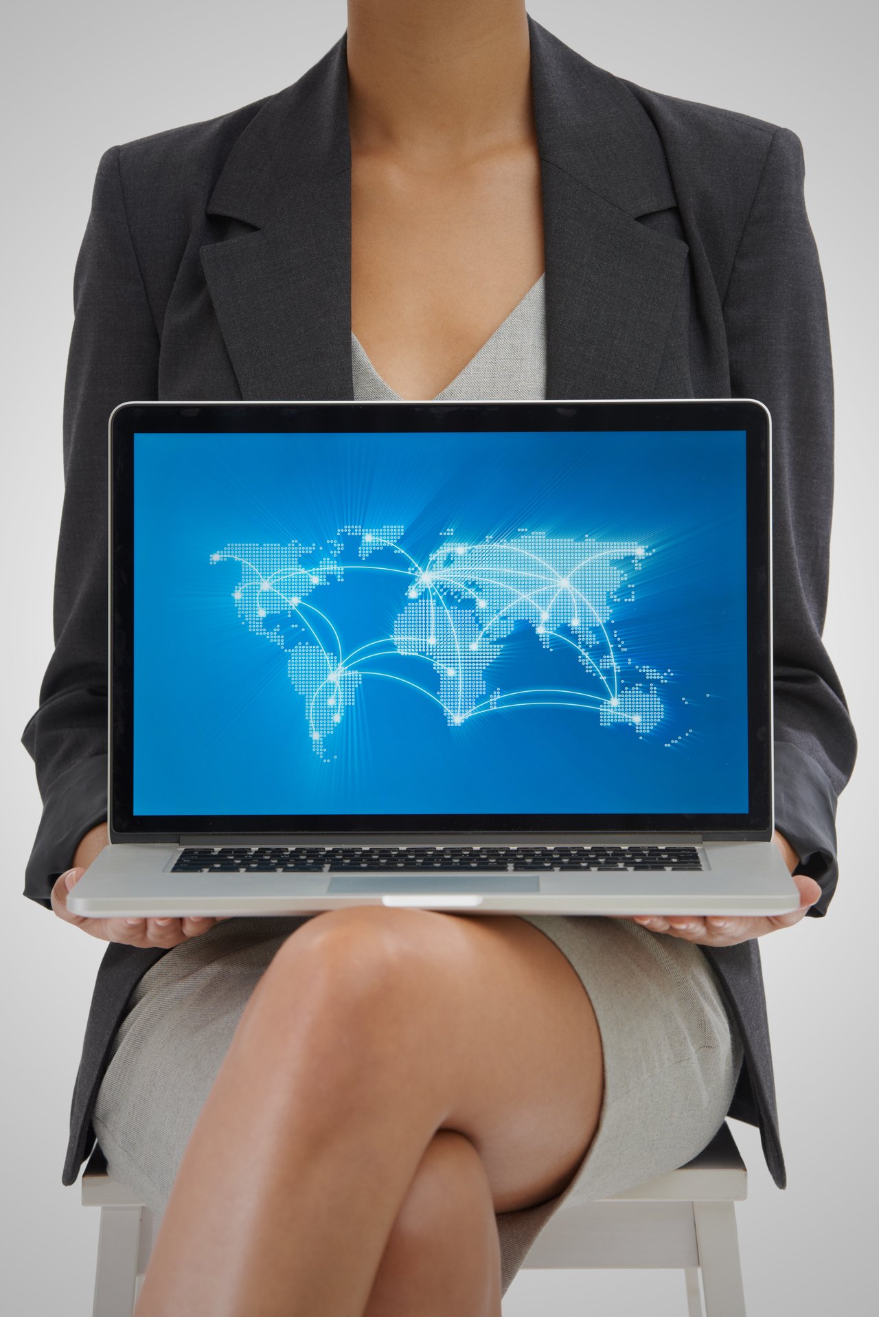 Eine Person im Business-Outfit hält einen Laptop mit einer Weltkarte und Verbindungslinien in den Händen.
