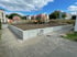 Baustelle mit gelbem Radlader hinter einer neuen Stützmauer aus Beton-L-Steinen neben einem gepflasterten Gehweg.