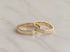 Zwei Eheringe aus Gelbgold auf Marmorgrund, ein Ring schlicht und einer mit umlaufendem Diamantbesatz.