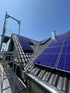 Dach mit grauen Ziegeln, Solarmodulen und Dachrinne; Gerüst links.