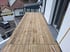Eine neu verlegte Holzterrasse aus hellbraunen Dielen vor einem weißen Haus mit Blick auf ein geparktes Auto.