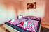 Schlafzimmer mit zwei Einzelbetten, rosa Bettwäsche, Nachttisch, Lampe und Rosenbild an der Wand.