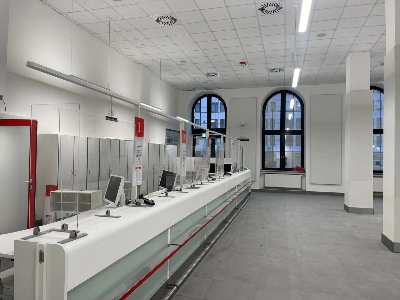 Leerer Schalterraum mit mehreren Computermonitoren und hohen Fenstern.