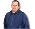 Ein lächelnder Mann in Arbeitskleidung steht hinter einem Holztisch mit Parkettmustern.