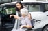 Eine Frau hilft einer älteren Frau aus einem Rollstuhl ins Auto.