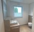 Modernes Badezimmer mit Waschbecken, hellbrauner Holzplatte, Fenster mit Jalousie und Toilette.
