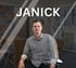 Junger Mann im gestreiften Hemd sitzt auf einem Stuhl vor einem unscharfen Büro, Text "JANICK".