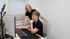 Zwei Frauen in schwarzer Kleidung arbeiten gemeinsam lächelnd an einem Computerbildschirm im Büro.
