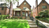 A two-story brick house with a front porch and steps leading up from a green lawn.