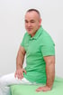 Ein lächelnder Mann in grünem Poloshirt und weißer Hose sitzt auf einer grünen Liege vor weißem Hintergrund.
