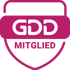 Rosa GDD MITGLIED-Schild auf dunkelgrünem Hintergrund.
