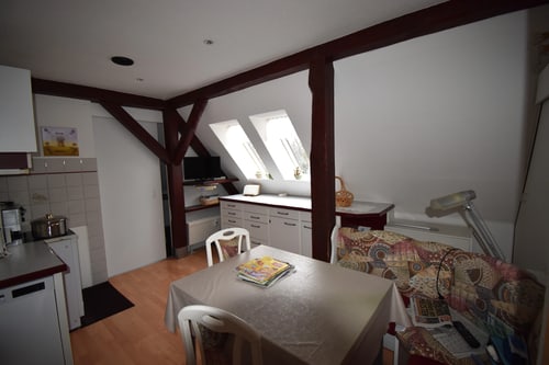 Dachbodenwohnung mit Holzbalken, zwei Dachfenstern, Esstisch mit Stühlen und einer Küchenzeile.