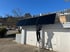 Mann auf Leiter installiert schwarze Solarpanels auf einem Garagendach unter blauem Himmel.