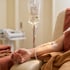 A person receives an IV drip labeled Cellular Therapy Solution through a catheter in their arm while resting in a clinic chair.