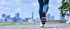 Beine einer joggenden Person in Sportkleidung auf einem Weg vor einer unscharfen Skyline mit grafischen Wellenlinien.