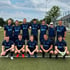 Eine Fußballmannschaft aus 11 Männern in dunkelblauen Trikots posiert auf einem grünen Rasenplatz.